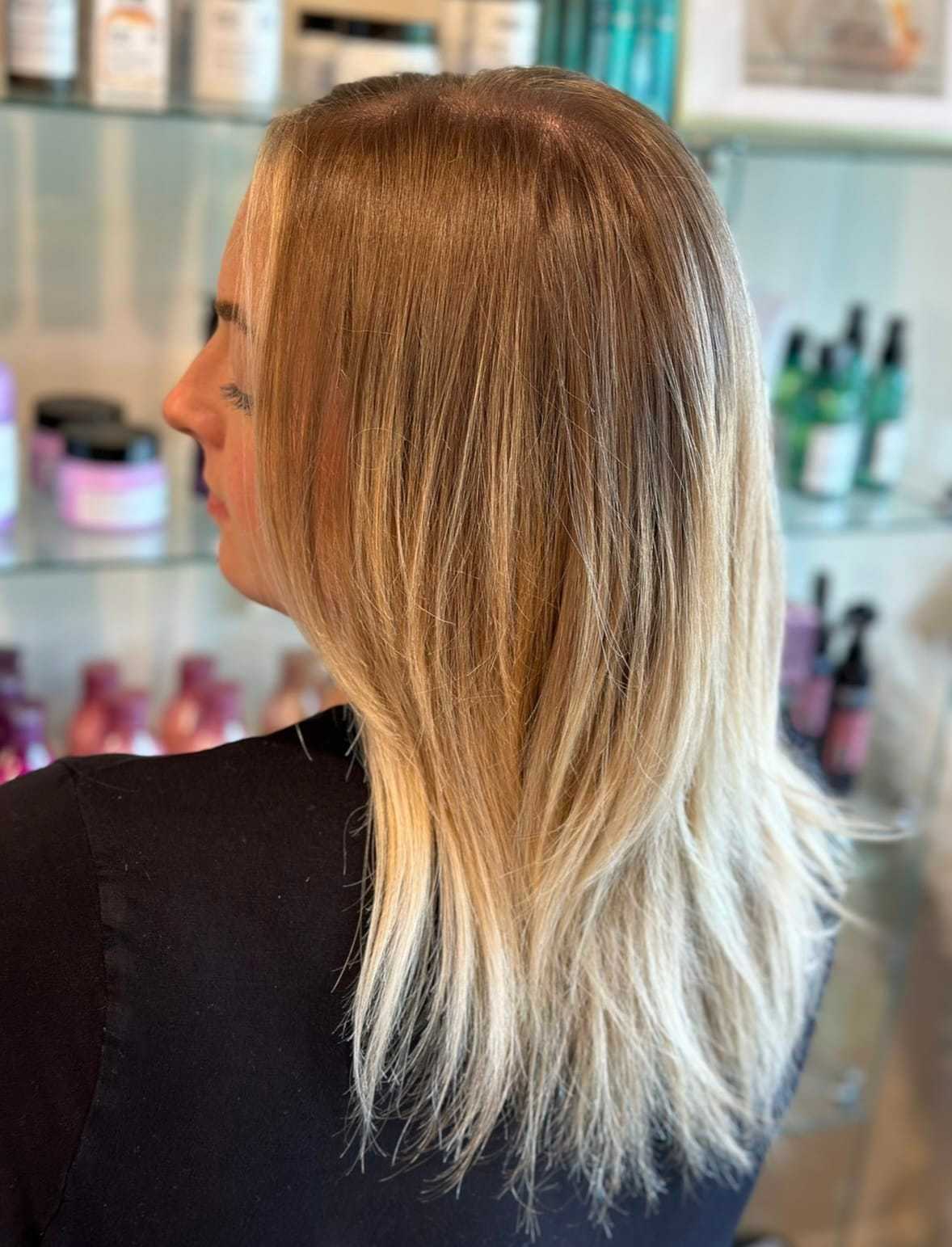 Blonde hair with layered cut in a salon setting, displaying various hair products.