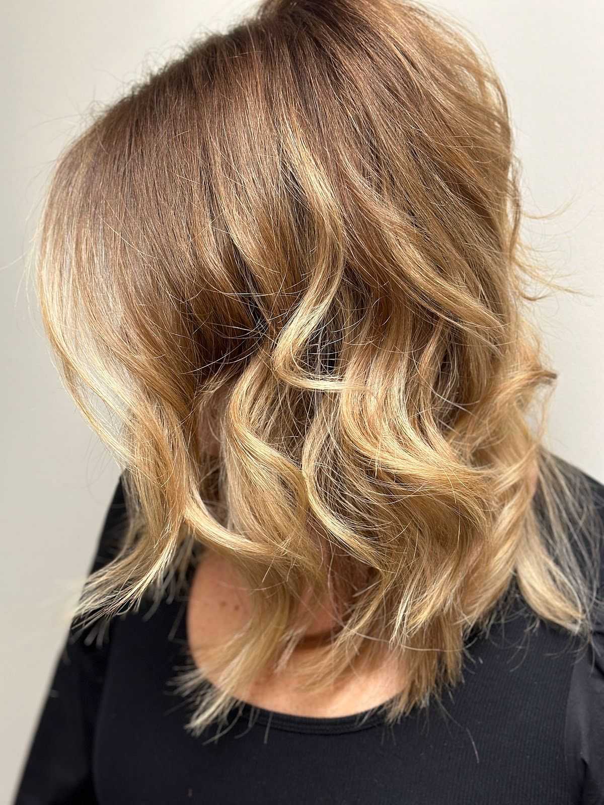 Woman with shoulder-length, wavy blonde hair, styled with beachy waves, wearing a black top.